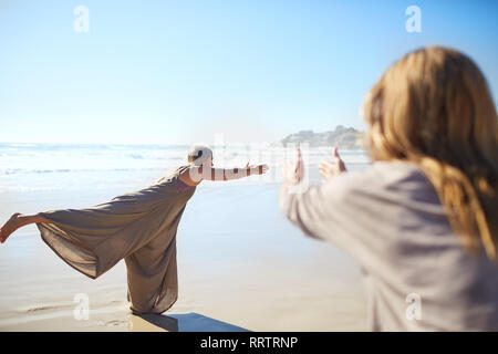 Woman practicing warrior 3 poser sur plage ensoleillée au cours de yoga retreat Banque D'Images