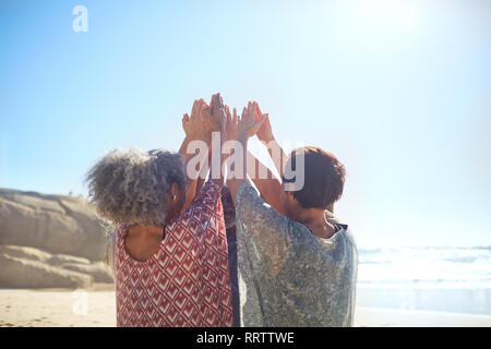 Les femmes avec bras levés en cercle sur la plage ensoleillée au cours de yoga retreat Banque D'Images