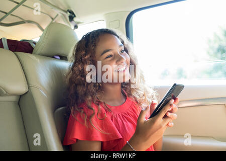 Tween Smiling girl using smart phone in back seat of car Banque D'Images