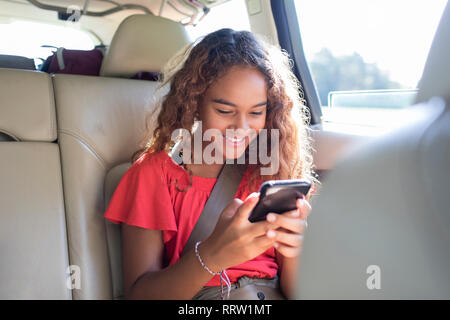 Le Tween girl using smart phone in back seat of car Banque D'Images