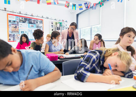 Aider les enseignants de sexe féminin junior high school girl les élèves à faire leurs devoirs at desk in classroom Banque D'Images