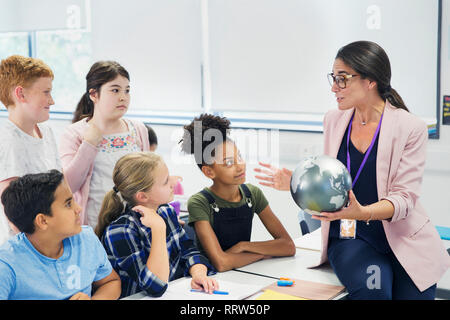 Attentifs junior high school students watching professeur de géographie avec globe Banque D'Images