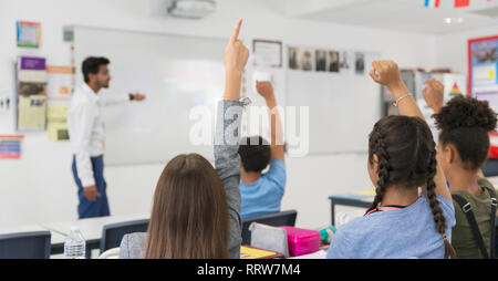 Des élèves du premier cycle du secondaire avec les mains levées pendant la leçon en classe Banque D'Images