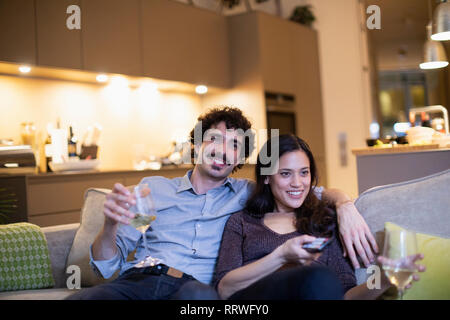 Heureux couple drinking white wine et regarder la télé sur canapé appartement Banque D'Images