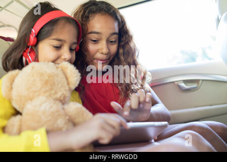 Sisters using digital tablet in back seat of car Banque D'Images