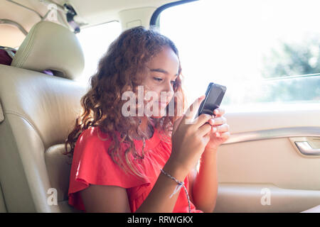 Le Tween girl using smart phone in back seat of car Banque D'Images