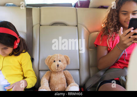 Les sœurs avec ours en peluche à l'aide de smart phone et digital tablet, équitation de siège arrière de voiture Banque D'Images