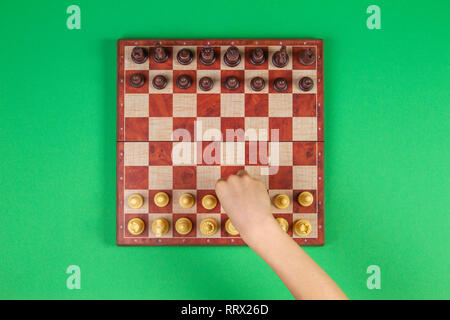 Kid mains sur un échiquier jouant aux échecs sur fond vert, vue du dessus Banque D'Images