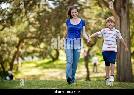 Garçon tenant la main de sa mère comme ils marchent à travers le parc. Banque D'Images