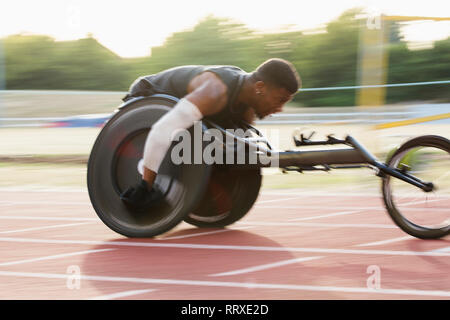 Déterminé jeune mâle athlète paraplégique en accélérant le long de la piste en course en fauteuil roulant de sport Banque D'Images