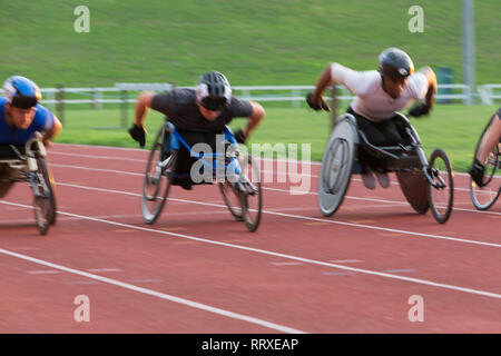 Déterminé athlète paraplégique en accélérant le long de la piste en course en fauteuil roulant de sport Banque D'Images