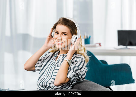 Happy blonde femme en chemise rayée à l'écoute au casque de la musique Banque D'Images