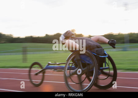 Athlète paraplégique en accélérant le long de la piste en course en fauteuil roulant de sport Banque D'Images
