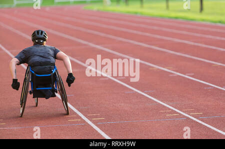 Femme athlète paraplégique en accélérant le long de la piste en course en fauteuil roulant de sport Banque D'Images