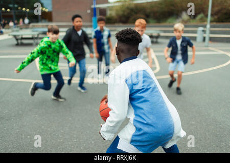 Le Tween garçons jouant au basket-ball dans la cour de l'école Banque D'Images