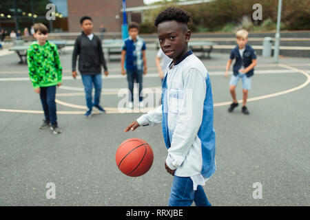 Portrait confiant tween Garçon jouant au basket-ball dans la cour de l'école Banque D'Images
