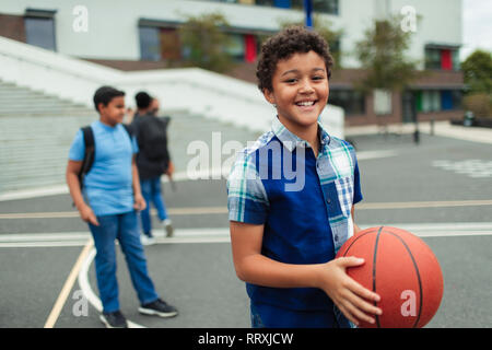 Portrait souriant, confiant le tween Garçon jouant au basket-ball dans la cour de l'école Banque D'Images