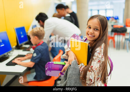 Portrait souriant, confiant junior high girl student portant des livres dans la bibliothèque Banque D'Images