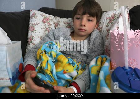 L'enfant malade sur le divan à regarder la télévision Banque D'Images