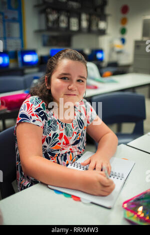 Portrait souriant, confiant junior high school girl writing in notebook in classroom Banque D'Images