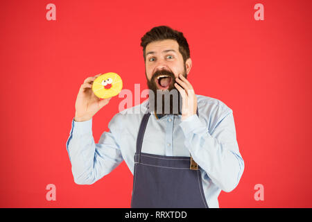 Faits sur le sucre. Aucun moyen. Barbu hippie baker tenir beigne glacé sur fond rouge. Cafe and Bakery concept. Sweet donut de Baker. Barbu homme Baker en tablier de cuisine tenir cute dessert. Banque D'Images