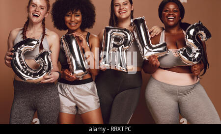 Groupe diversifié de femmes girl mot dans les lettres de ballon sur fond brun. Portrait of smiling girls avec différents organes se tenant ensemble. Banque D'Images