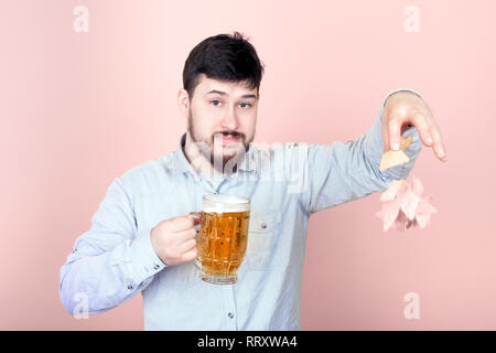 Homme barbu mignon avec un verre de bière chute des nachos, image sur un fond rose Banque D'Images