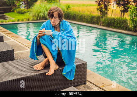 Homme malade de voyageur. L'homme a attrapé un rhume en vacances, se trouve triste à la piscine, boire du thé et souffle son nez dans un linge. Son fils est en bonne santé et Banque D'Images