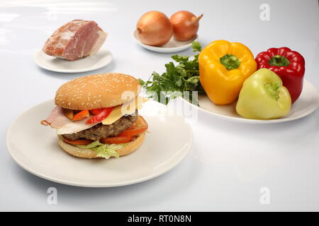 Cheeseburger avec bacon et boeuf patty sur une assiette de légumes, poivrons, tomates, oignons, concombres, persil et de la salade sur un fond blanc, s Banque D'Images