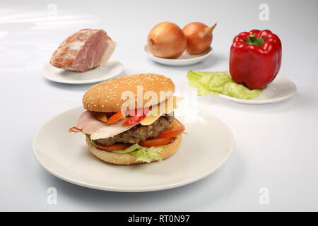 Cheeseburger avec bacon et boeuf patty sur une assiette de légumes, poivrons, tomates, oignons, concombres, persil et de la salade sur un fond blanc, s Banque D'Images