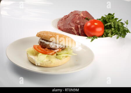 Cheeseburger avec bacon et boeuf patty sur une assiette de légumes, poivrons, tomates, oignons, concombres, persil et de la salade sur un fond blanc, s Banque D'Images