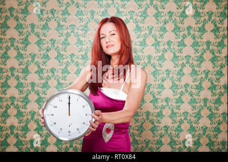 Frau dans violettem Abendkleid mit roten langen Haaren vor barocker haelt Tapete eine Uhr auf die punkt 12 Uhr steht in der Hand. [(C) Dirk A. Friedrich Banque D'Images