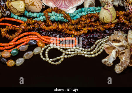 Vieux lumineux de perles turquoise, corail rouge, orange, grenade, agate colorée, perles parmi les bourgeons secs et coquilles sur fond noir Banque D'Images