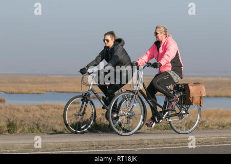 Southport, Merseyside. 27 février 2019. Météo britannique. Le soleil voilé commence à la journée à Marshside nature Reserve, avec deux femmes cyclistes qui profitent d'un sprint sur le Pennine Way Cycway qui donne généralement de bonnes vues sur un Blackpool hazy. Les prévisions sont pour un autre après-midi sec et ensoleillé sur la côte nord-ouest, et continue insaison doux. Crédit: MWI/AlamyLiveNews crédit: MediaWorldImages/Alay Live News Banque D'Images