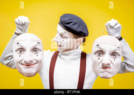 Portrait d'un pantoomime tenant deux masques visage avec différentes émotions sur le fond jaune. Concept de split de la personnalité Banque D'Images