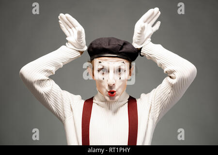 Portrait d'un acteur de pantomime avec maquillage du visage blanc posant avec l'expression des émotions sur l'arrière-plan gris à l'intérieur Banque D'Images