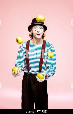 Maquillage du visage blanc avec pantomime à jongler avec des pommes sur le fond rose en studio Banque D'Images