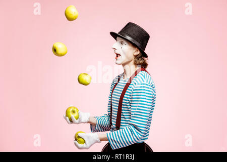 Maquillage du visage blanc avec pantomime à jongler avec des pommes sur le fond rose en studio Banque D'Images