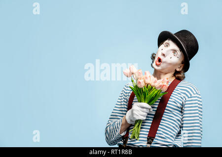 Pantomime émotionnelle posant avec un bouquet de tulipes sur fond bleu à l'intérieur. La Saint-Valentin et l'amour concept Banque D'Images