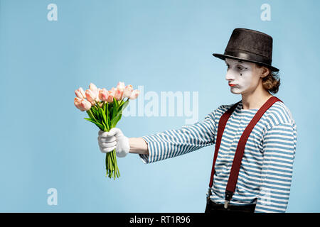 Pantomime émotionnelle posant avec un bouquet de tulipes sur fond bleu à l'intérieur. La Saint-Valentin et l'amour concept Banque D'Images