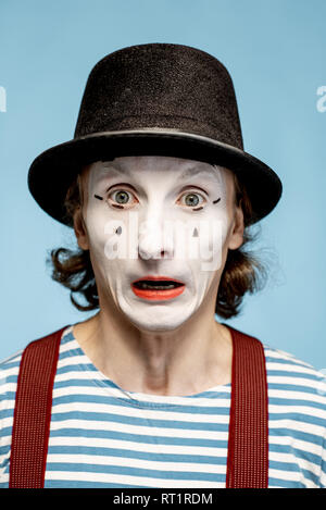 Portrait en gros plan d'un acteur comme une pantomime avec blanc maquillage du visage montrant l'expression des émotions sur le fond bleu Banque D'Images