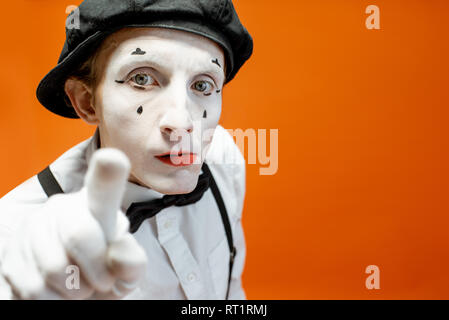 Portrait d'un acteur comme une pantomime avec blanc maquillage du visage montrant l'expression des émotions sur fond orange dans le studio Banque D'Images