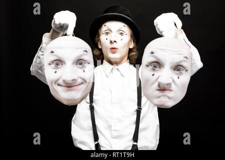 Portrait d'un pantoomime tenant deux masques visage avec différentes émotions sur le fond noir. Concept de split de la personnalité Banque D'Images