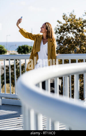 Smiling woman sitting on a bridge selfies Banque D'Images