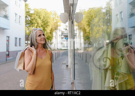 Portrait of smiling woman carrying shopping bags à la vitrine en Banque D'Images