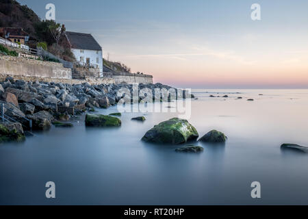 Ancienne maison du garde-côtes (et blanchis à la chaux et au toit de chaume) se trouve au-dessus de la mer, par le mur du port et sous des falaises - Runswick Bay, Angleterre, Royaume-Uni. Banque D'Images