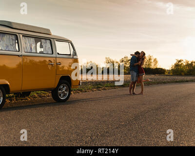 Couple heureux de faire un voyage sur la route avec un camping-car, rire et embrassant sur la route Banque D'Images