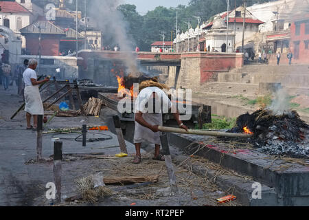 Les hommes de la caste hindoue (Dom) d'attiser par les bûchers funéraires de la rivière Bagmati au motif de temple de Pashupatinath, Katmandou, Népal Banque D'Images