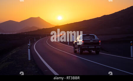 Voiture sur une route sinueuse de la conduite vers le coucher du soleil. Lanzarote Banque D'Images