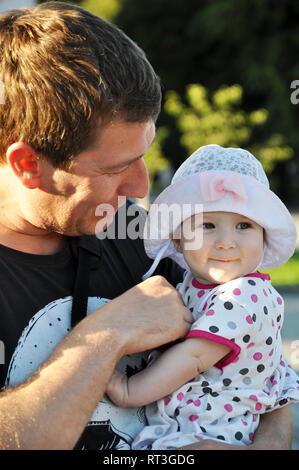 Cute smiling little girl in a hat dans les bras de son père marcher sous le soleil de jour d'été. Banque D'Images